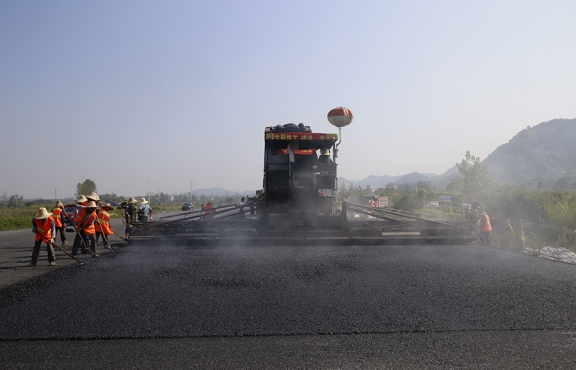 2019年8月，宜春經(jīng)開區(qū)S311路面攤鋪現(xiàn)場，工友們輔助路面兩側(cè)的分料、補(bǔ)窩等作業(yè)